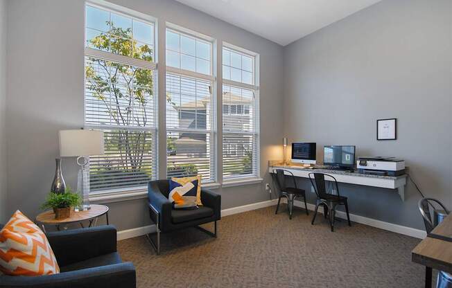 A room with a desk, chairs, and a couch with a window in the background.