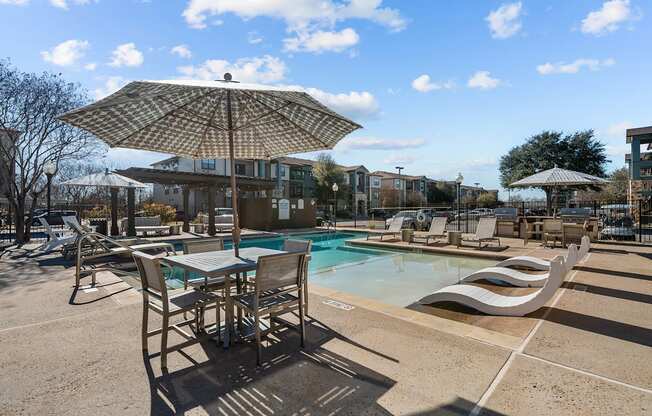 A sunny day at the pool with chairs and an umbrella.