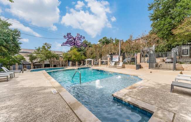 a swimming pool with a fountain and a fence with trees