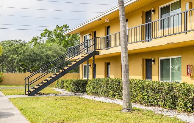 a yellow house with a staircase and a grass yard