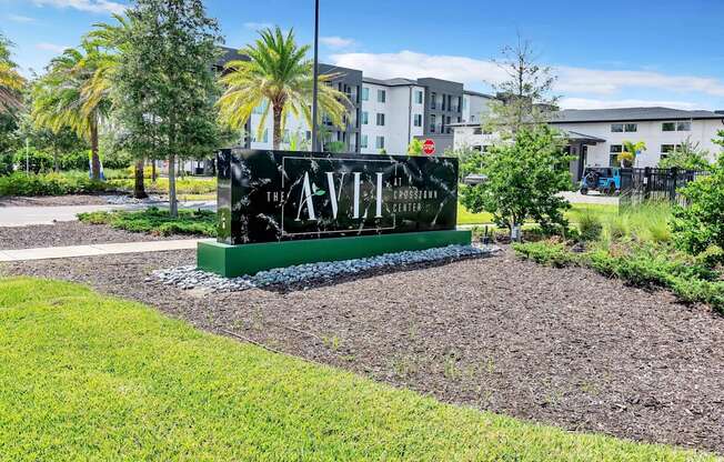 a sign in the middle of a grassy area with buildings in the background