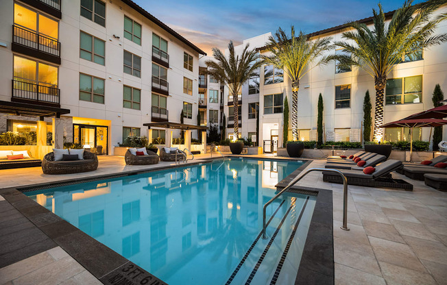 Sparkling pool surrounded by lounge seating, modern cabanas, and softly lit palm trees