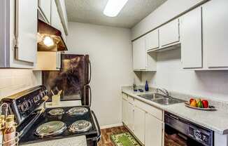 Apartments in Fort Worth TX - Monarch Pass - Kitchen with Wood-Style Floor, Black Appliances, Wooden Cabinets, and Double-Sink with Speckled Countertop