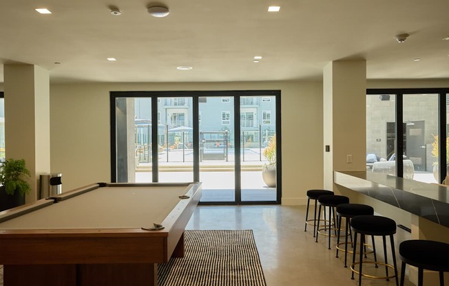A pool table is in the middle of a room with bar stools.