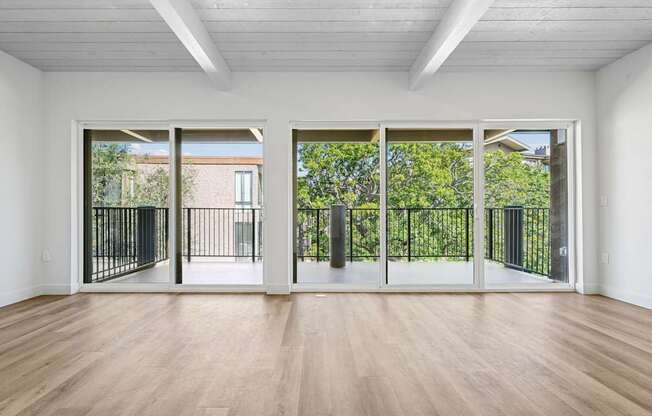 A room with white walls and wooden flooring, and three sliding glass doors.