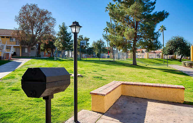 A black mailbox sits on a pole next to a brick bench in a sunny park.