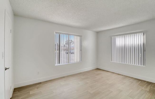 A room with wooden flooring and two windows with blinds.