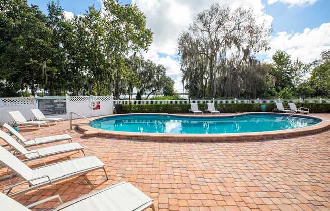 A pool surrounded by trees and chairs.