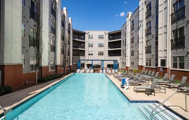 a swimming pool with lounge chairs in front of an apartment building
