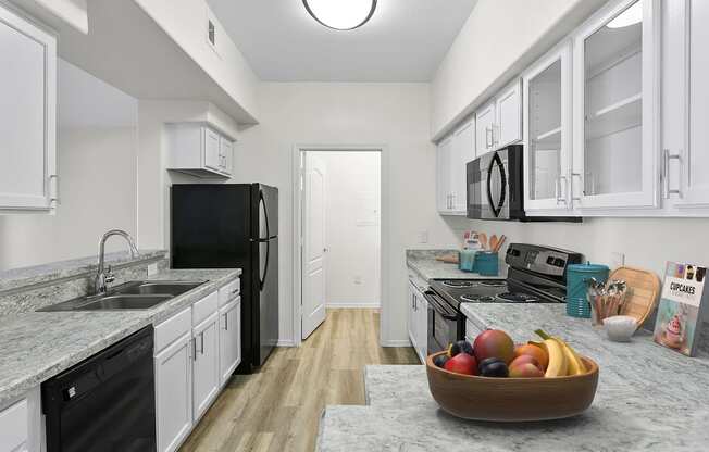 a kitchen with white cabinets and black appliances and a bowl of fruit