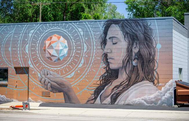 A mural of a woman holding a geometric object is painted on a building.