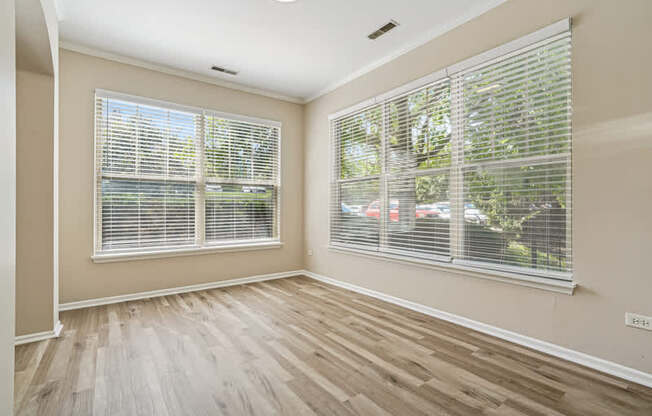 A room with wooden floors and two windows covered with blinds.