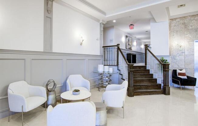 a lobby with white chairs and a staircase in the background