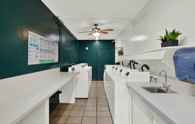 a laundry room with a row of sinks and a ceiling fan at Olive Tree Apartments, California