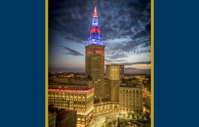 A cityscape with a tall building lit up in red, white and blue.