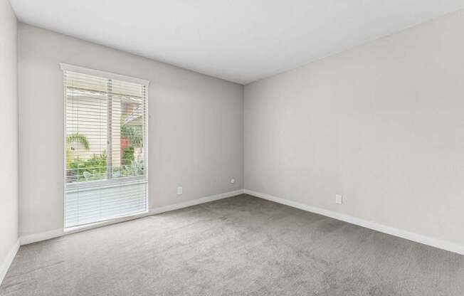 A room with a window and a view of a building and trees outside.
