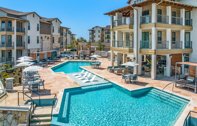 a swimming pool with chairs and umbrellas in front of an apartment building