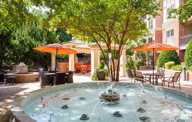 A fountain in the middle of a patio surrounded by chairs and umbrellas.
