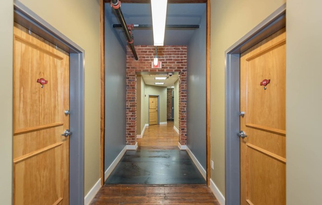 a hallway with wooden doors and a brick wall at Mayton Transfer Lofts, Petersburg, VA