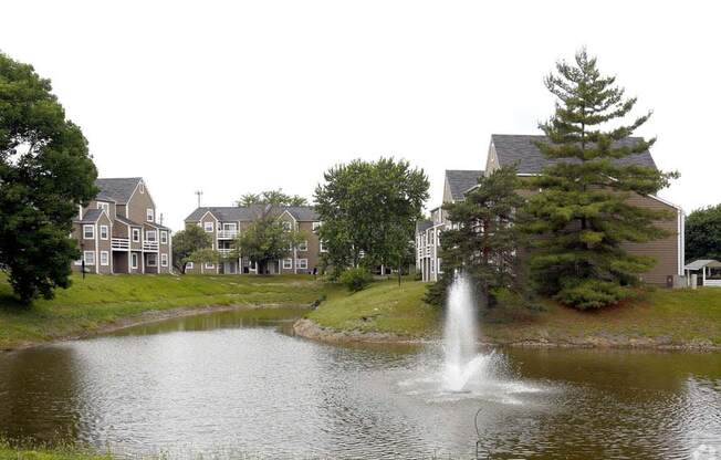 a fountain in a pond with houses in the background