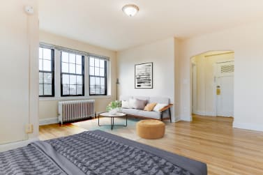 studio bedroom area with bed, nightstands, large windows and view of living area at the dahlia apartments in washington dc