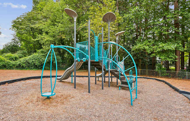 A playground with a teal slide and a brown ground.