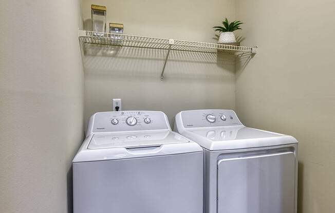 a washer and dryer in a laundry closer with a shelf above them at Wynnwood Vinings apartments