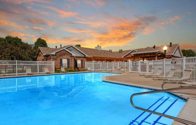 A large swimming pool in front of a house with a sunset in the background.
