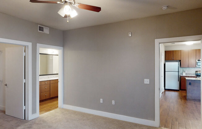 A room with a ceiling fan and a kitchen in the background.