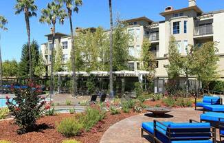 a courtyard with blue benches and trees in front of an apartment building