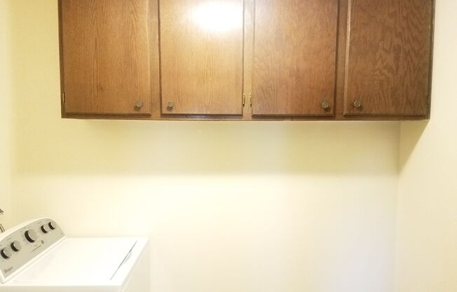 A white washing machine sits under a wooden cabinet.
