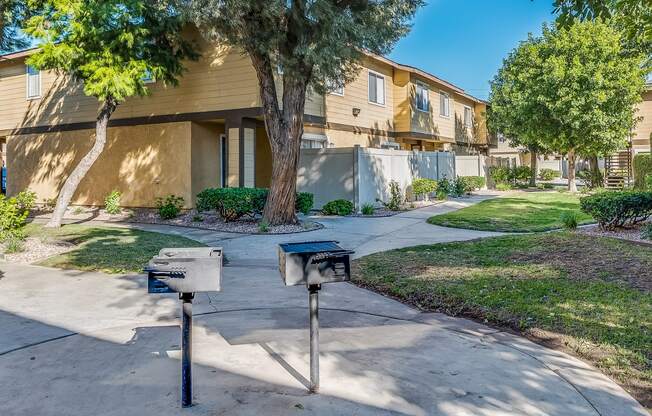 two bbq pits sit in the middle of a sidewalk in front of a yellow apartment