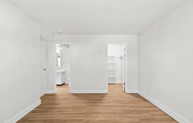A long, narrow, white hallway with wood floors and white walls.