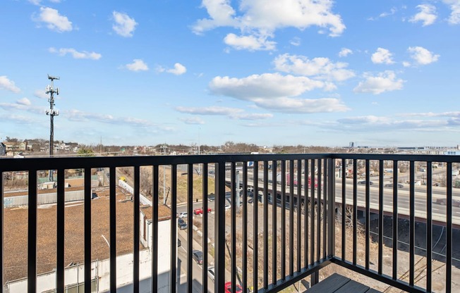A balcony with a black railing overlooks a parking lot and a road.