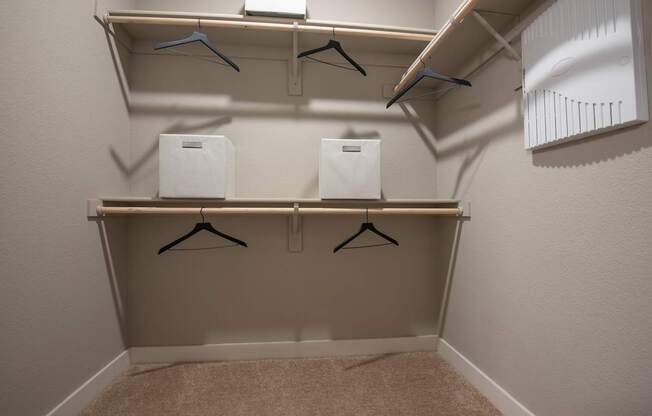A small closet with two shelves and three hangers.