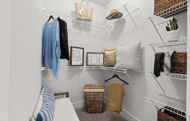 A white closet with clothes and baskets on the shelves.