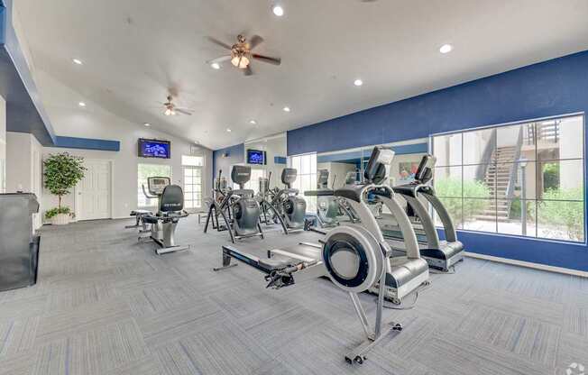 A gym with a variety of exercise equipment and a ceiling fan.