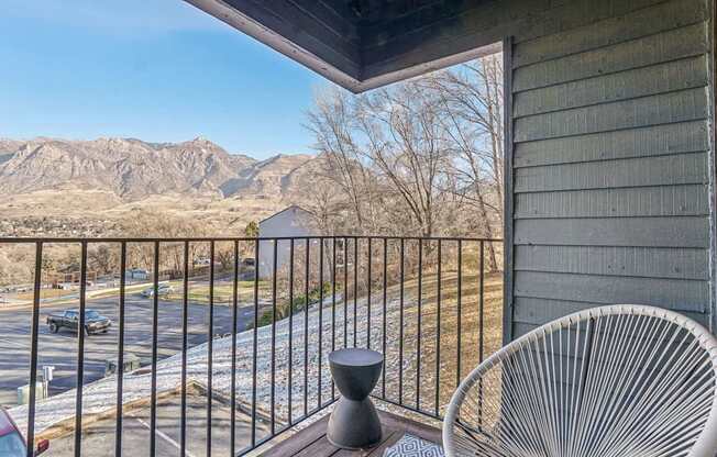 A chair is on a balcony overlooking a parking lot and mountains.