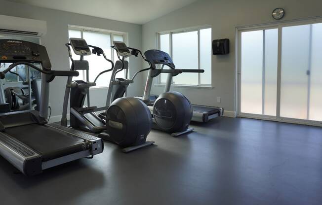 a gym with cardio equipment on the floor and large windows