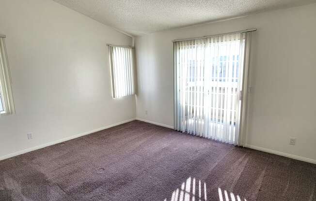 Large carpeted bedroom with private porch and lots of natural light at Northwoods Apartments in Upland, California.