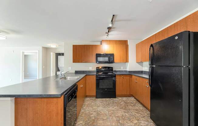 A black refrigerator is in the corner of a kitchen with wooden cabinets.