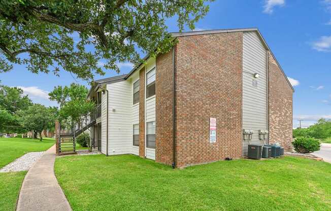 An apartment building with white wood and brick siding is surrounded by a lush grassy area at Estelle Creek North Apartments in Irving, TX