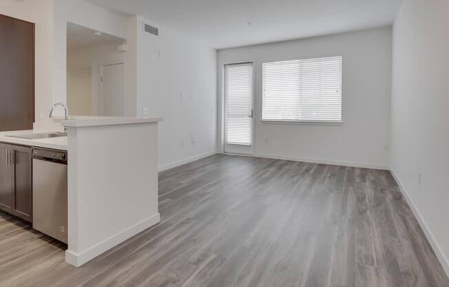 an empty living room with a kitchen in the background