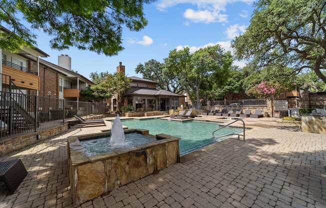 A pool with a fountain in the middle of a brick patio.