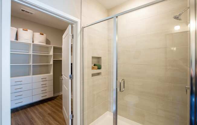 a walk in shower with a glass door and a closet with white shelves