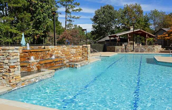 A large swimming pool with a stone wall and a small gazebo in the background.