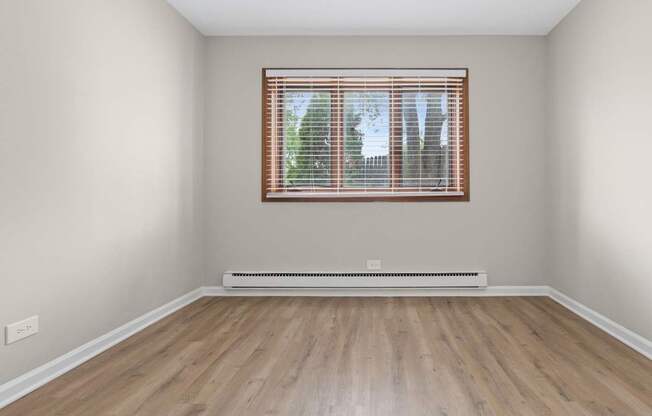 A room with a window and a radiator on a wooden floor.