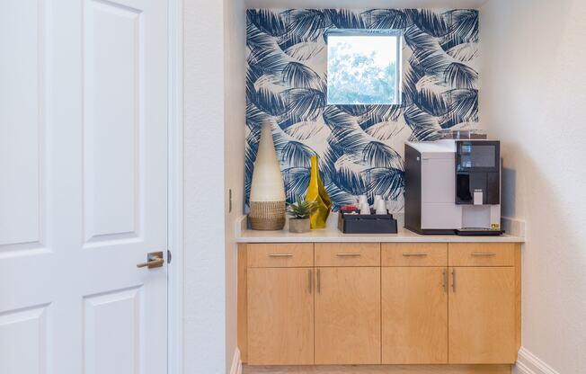 a kitchenette with a coffee machine and a mirror with a palm leaf pattern on the wall
