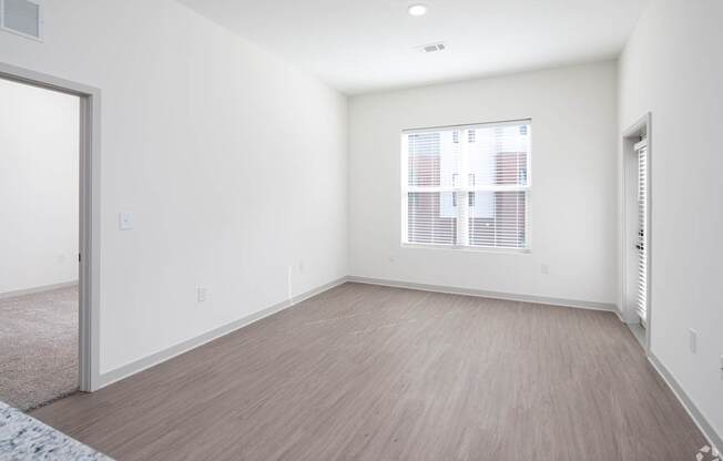 A room with a window covered by blinds and a wooden floor.