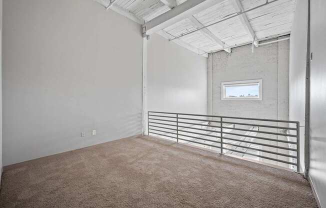 A room with a carpeted floor and a window with a metal railing.